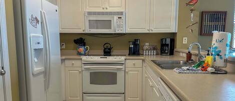 A kitchen with white cabinets, a microwave, a stove, a dishwasher, and various kitchen items on the counter.