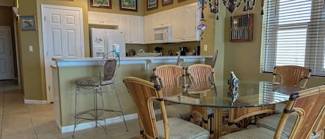 A kitchen with white cabinets, a refrigerator, a microwave, and a dining area with a glass table and wicker chairs.