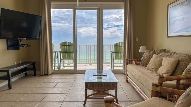 A living room with a TV, a glass-top coffee table, a sofa, and a view of the ocean through large sliding glass doors. - Spacious 3-bedroom Beachfront Condo Pool, Large Balcony (Pensacola)