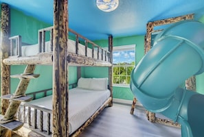 Una cama litera con tobogán, una ventana con vistas y una pared verde.