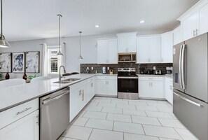 Una cocina moderna con armarios blancos, electrodomésticos de acero inoxidable y piso de baldosas.