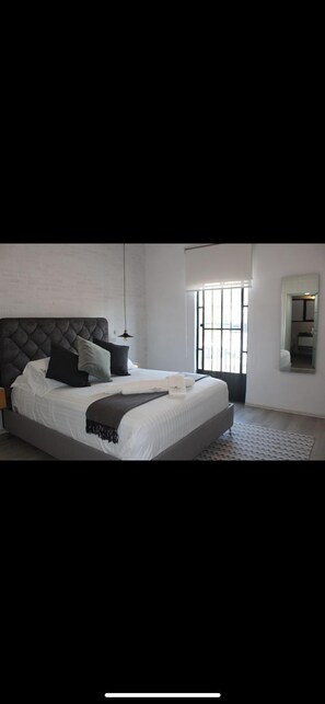 A modern bedroom with a large bed, a hanging light, and a view of the outdoors through a window. - JEES B&B (Mexico City)