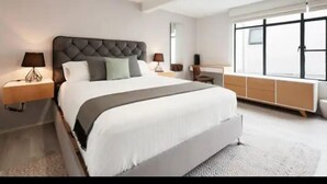 A modern bedroom with a large bed, bedside tables, a dresser, and a large window. - JEES B&B (Mexico City)