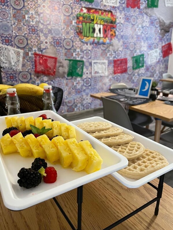 A tray of pineapple chunks, blackberries, raspberries, and waffles on a table in a room with a colorful wall and a sign that reads "Viva Mexico". - JEES B&B (Mexico City)