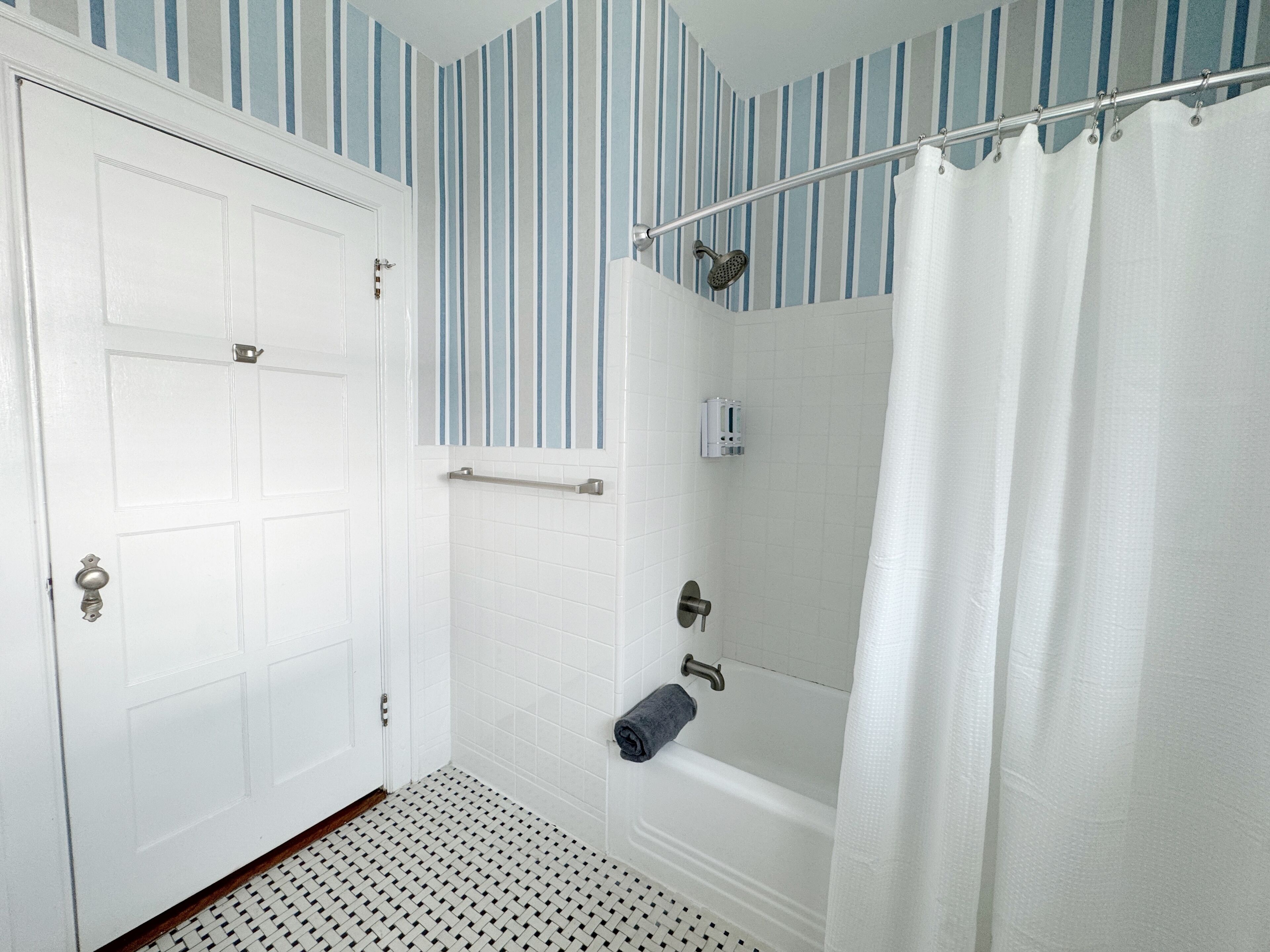 Un baño con una puerta blanca, una ducha con cortina y piso de baldosas.