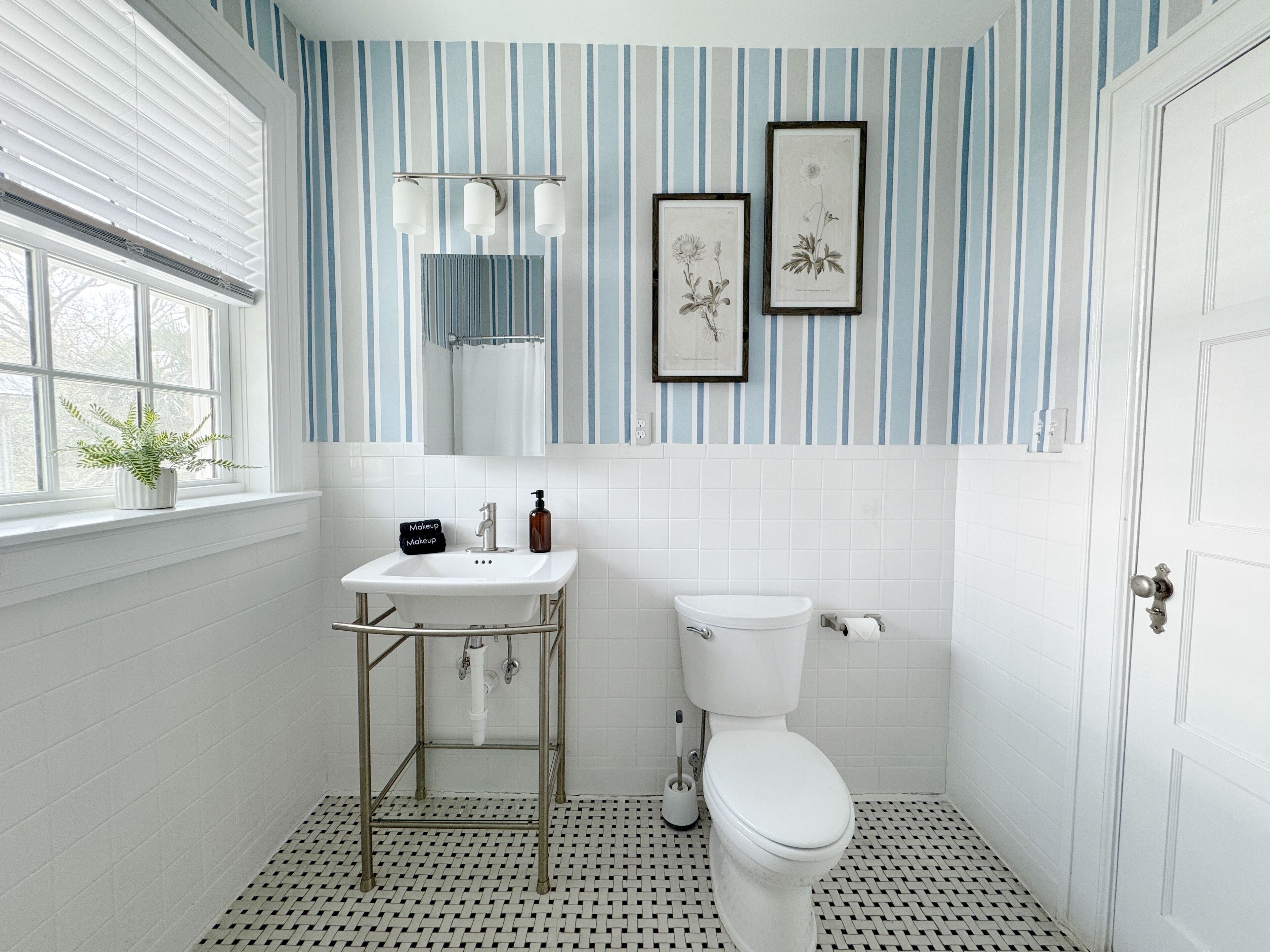 A bathroom with a white sink, a toilet, a window with blinds, and a potted plant.