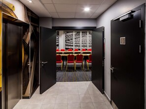Un salón de conferencias con mesas y sillas, un amplio ventanal con vistas, y una puerta con un letrero.