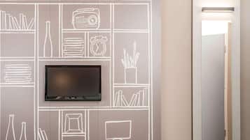 A modern room with a flat-screen TV mounted on a chalkboard wall, a door with a mirror, and a hallway.