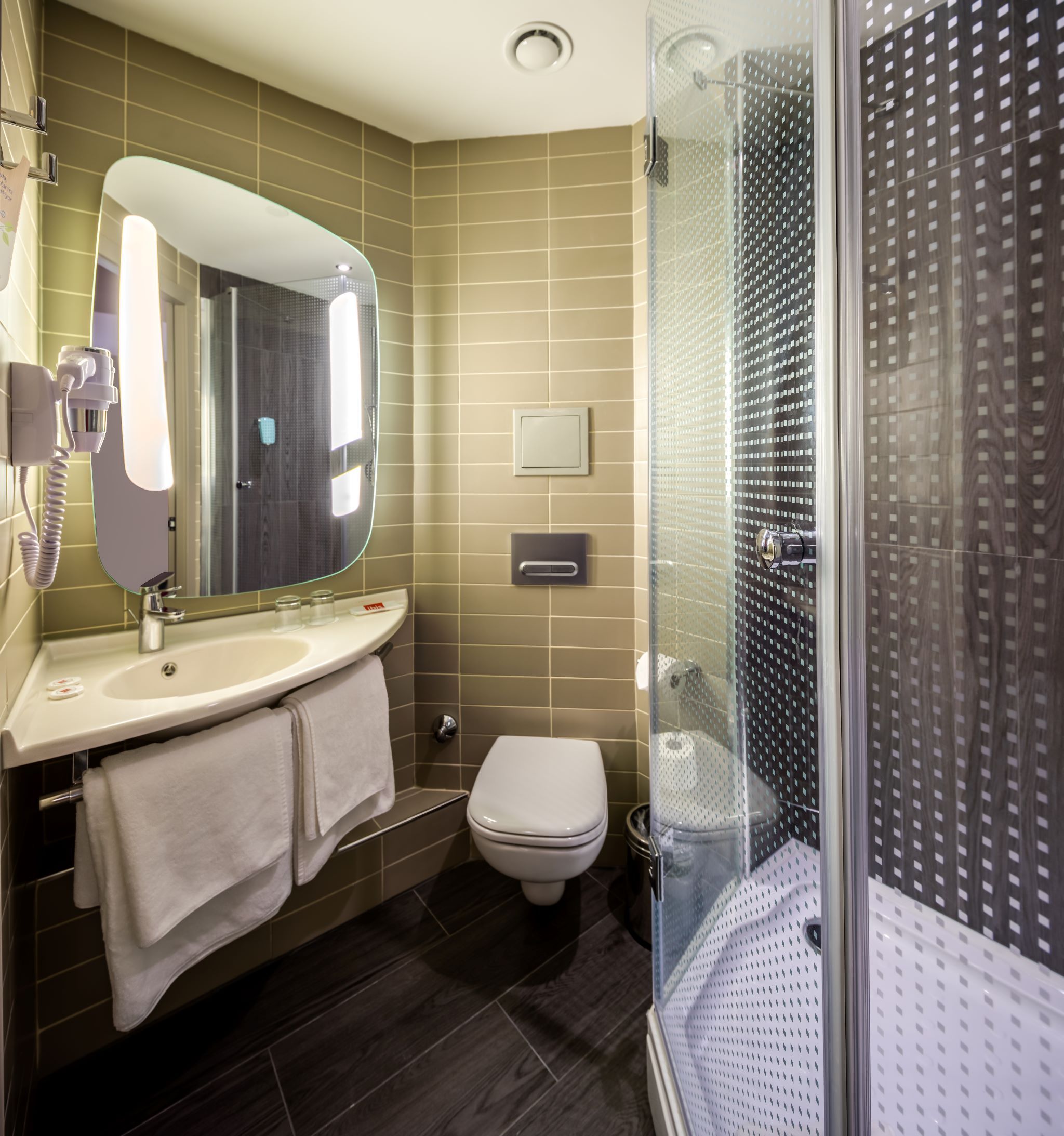 A modern bathroom with a large mirror, a sink, a toilet, and a glass-enclosed shower.