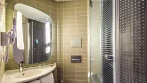 A modern bathroom with a large mirror, a sink, a toilet, and a glass-enclosed shower. - Ibis Istanbul West (Istanbul)