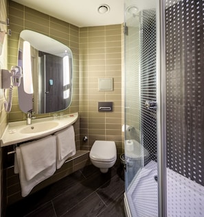 A modern bathroom with a large mirror, a sink, a toilet, and a glass-enclosed shower. - Ibis Istanbul West (Istanbul)