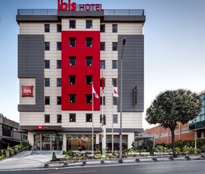 En modern hotellbyggnad med en framträdande röd och grå fasad, många fönster och en väl synlig entré.