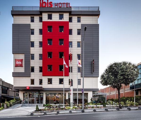 A modern hotel building with a prominent red and grey facade, multiple windows, and a visible entrance. - Ibis Istanbul West (Istanbul)