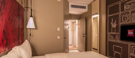A hotel room with a bed, a wall-mounted TV, a red textured wall, and a hallway leading to another room.