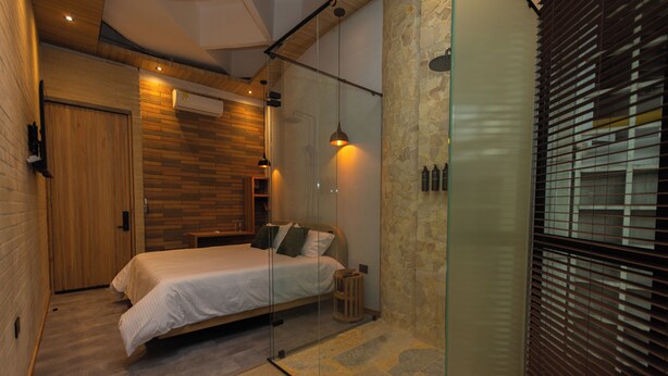 Une chambre moderne avec un lit, une armoire en bois, une cloison en verre et un mur en pierre.