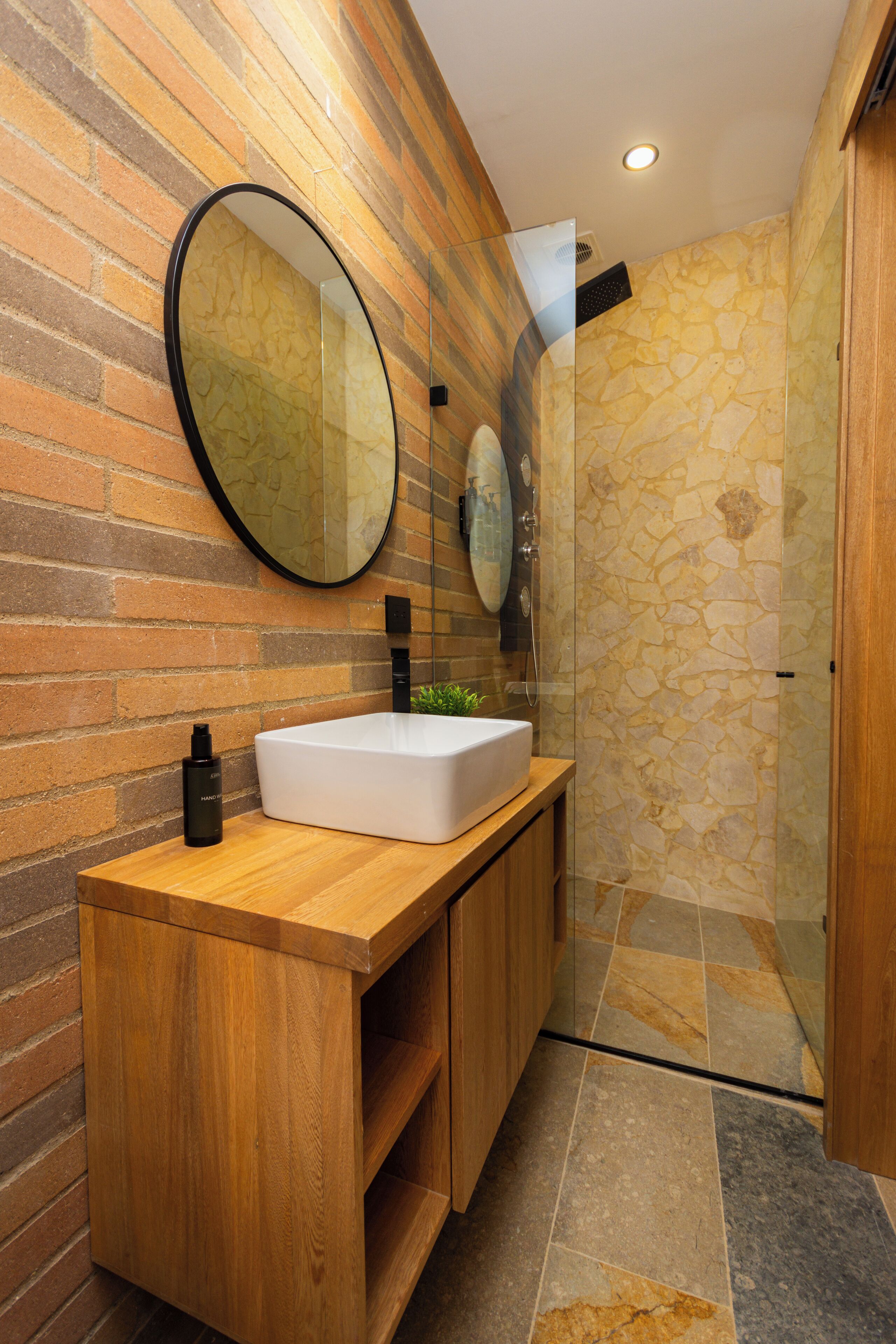 A modern bathroom with a wooden vanity, a large mirror, and a stone shower enclosure.