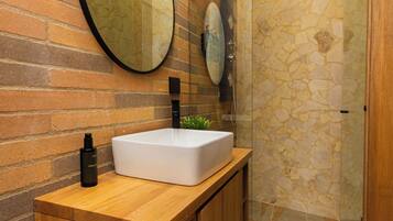 A modern bathroom with a wooden vanity, a large mirror, and a stone shower enclosure.