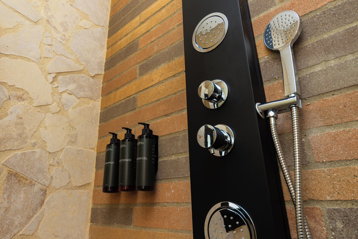 Ein modernes Duschgehäuse mit gebogenem schwarzen Design, einer Handbrause und drei Flaschen Shampoo und Conditioner.