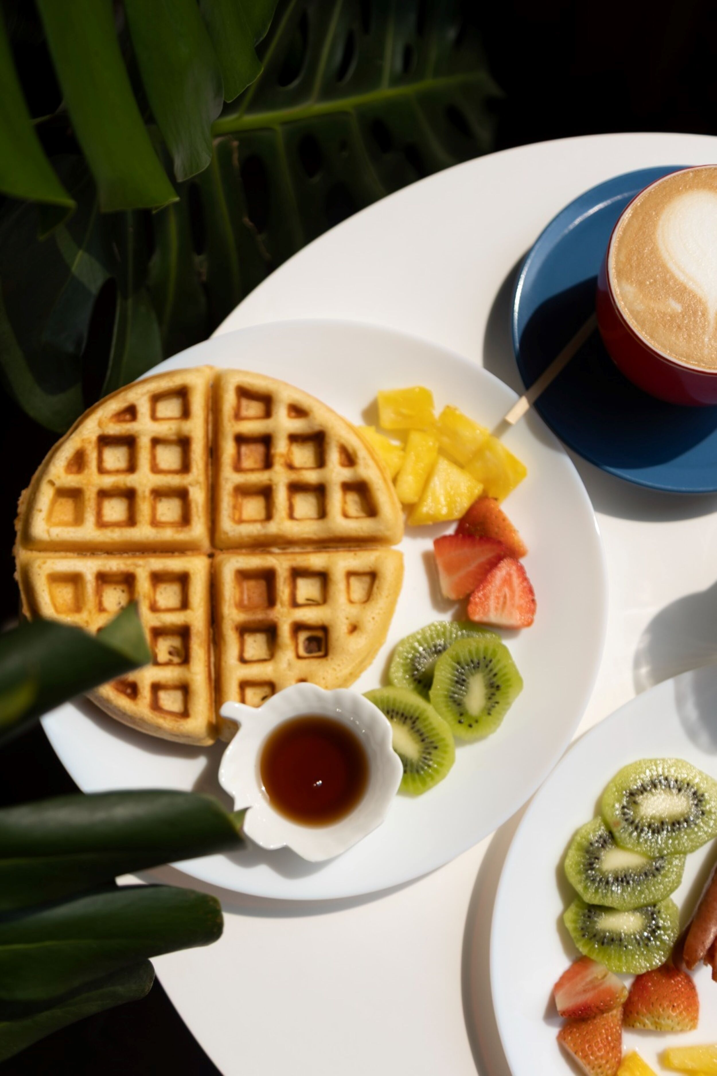 Un plato de desayuno con gofres, fruta y una taza de café.