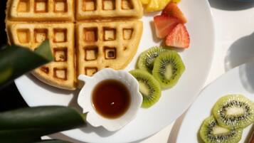 Un plato de desayuno con gofres, fruta y una taza de café.