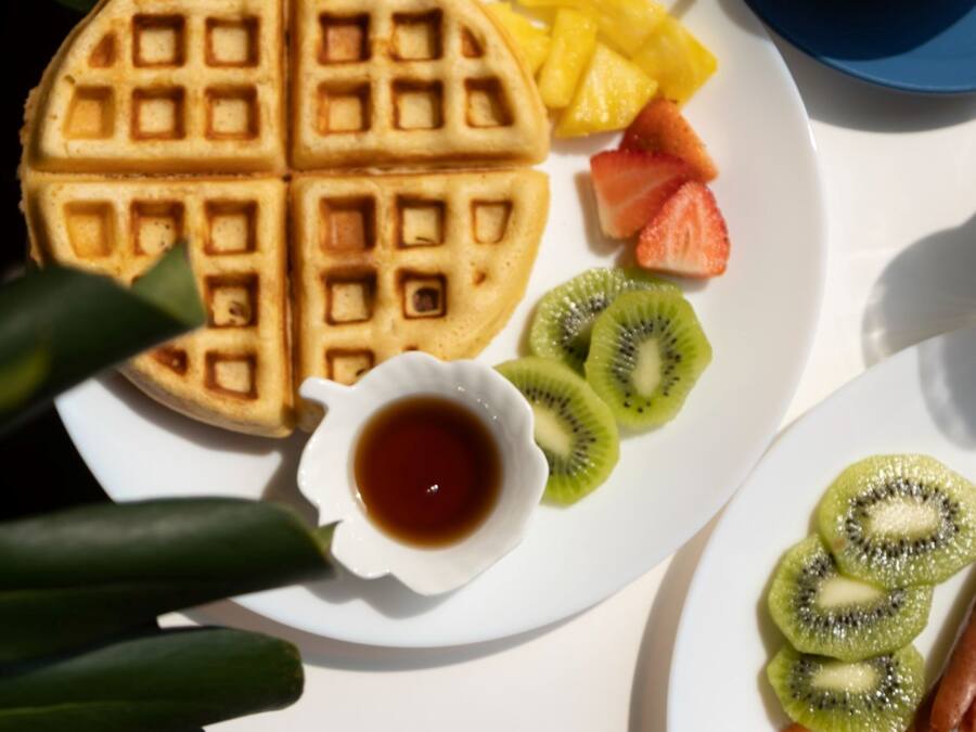 Un plato de desayuno con gofres, fruta y una taza de café.