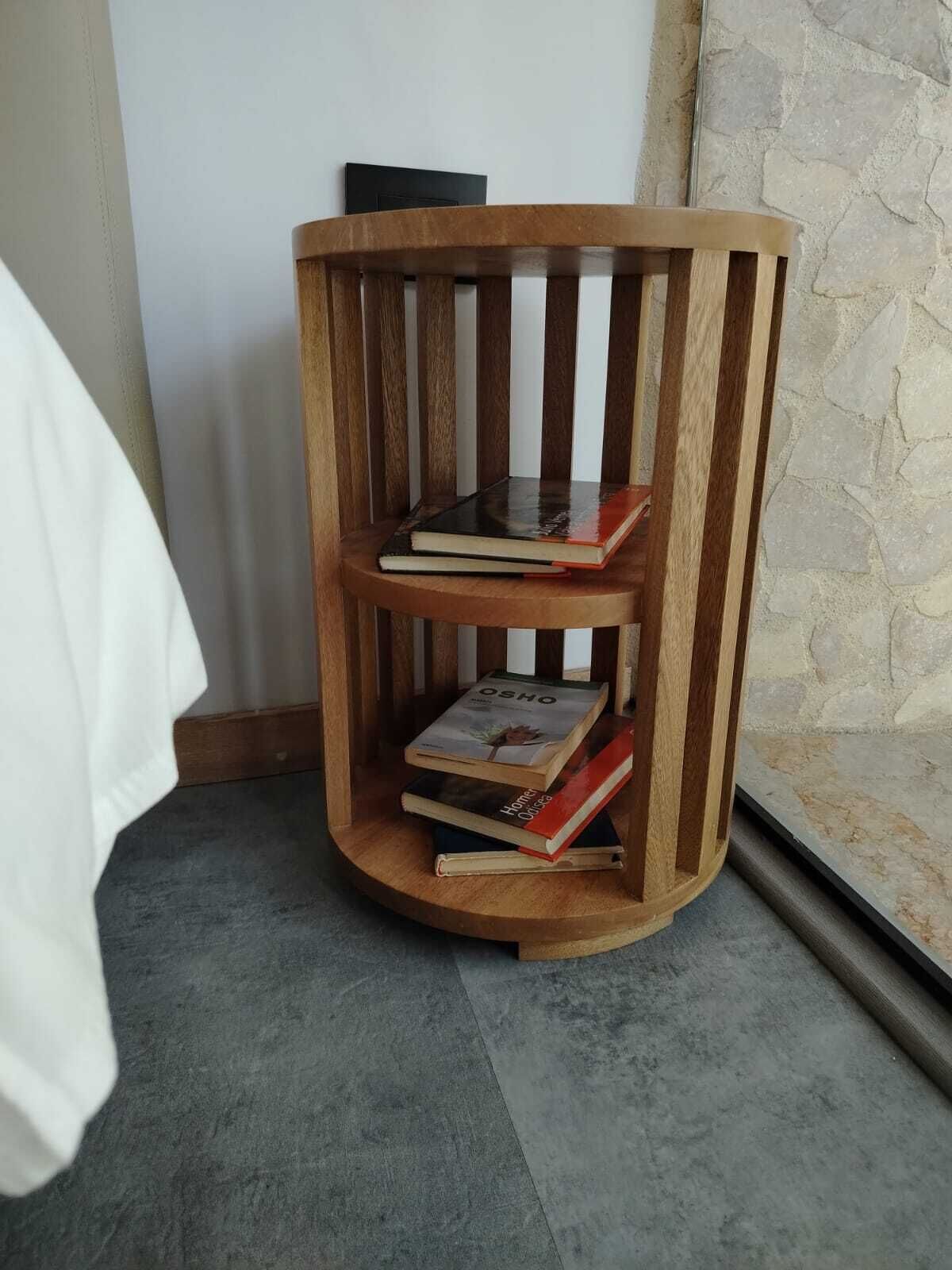 A wooden bookshelf with three shelves, a white wall, and a stone wall in the background.