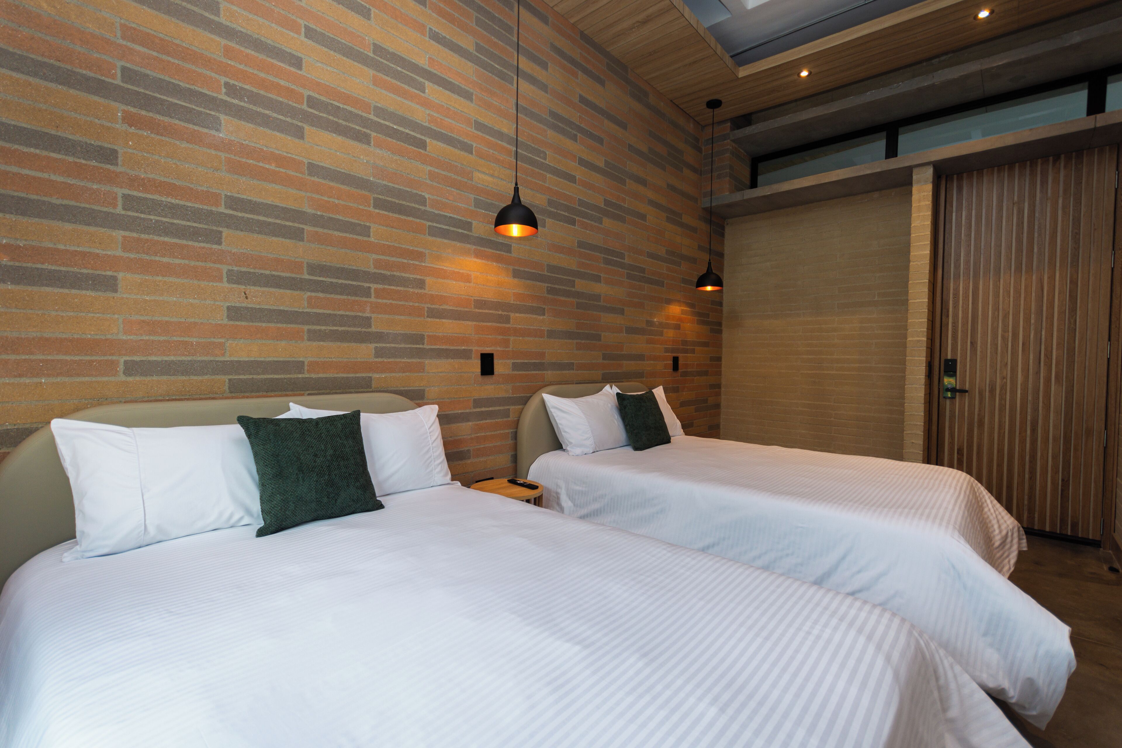A hotel room with two beds, a brick wall, wooden ceiling, and a sliding door.