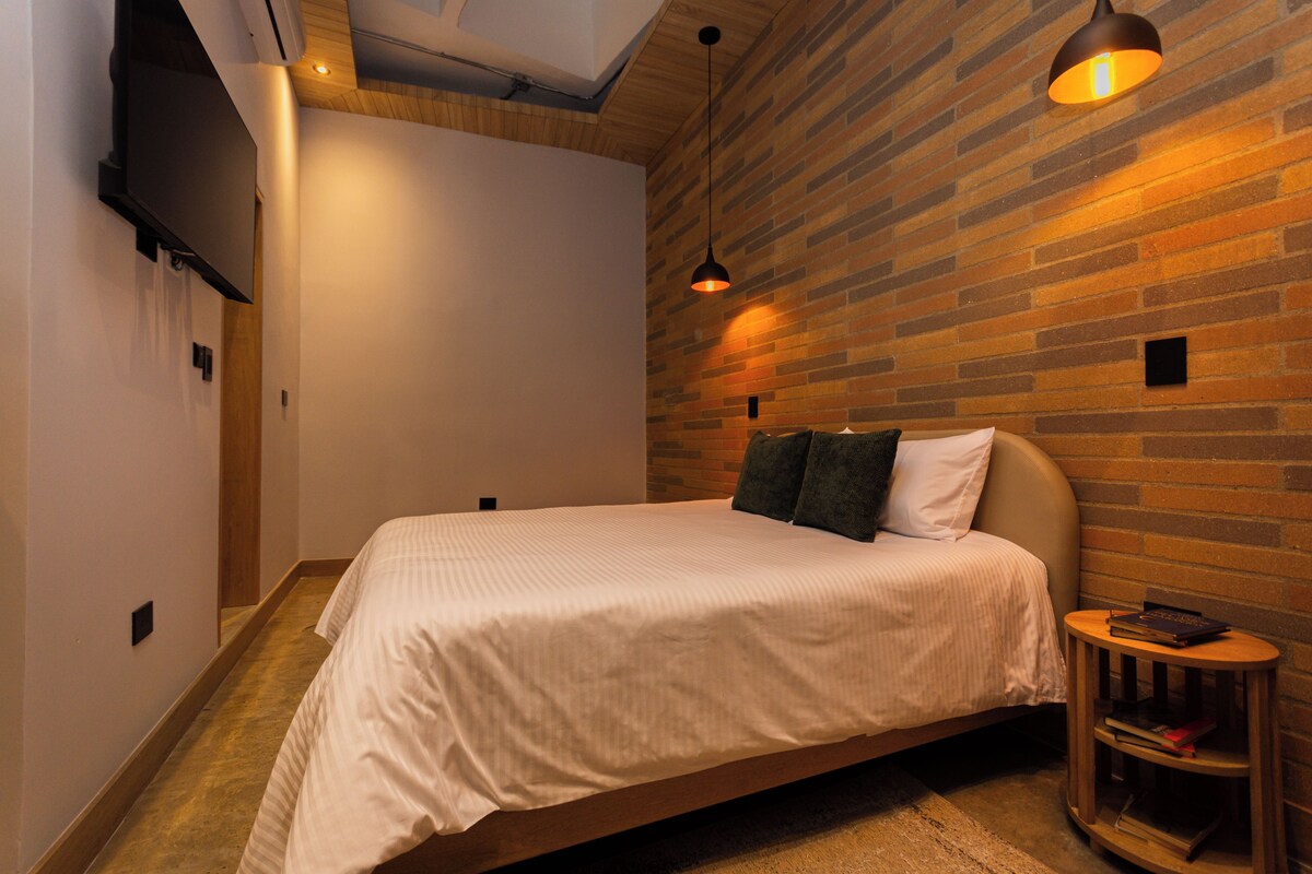 Une chambre à coucher moderne avec un grand lit, un mur d’accent en bois, une petite table de chevet et un luminaire suspendu.