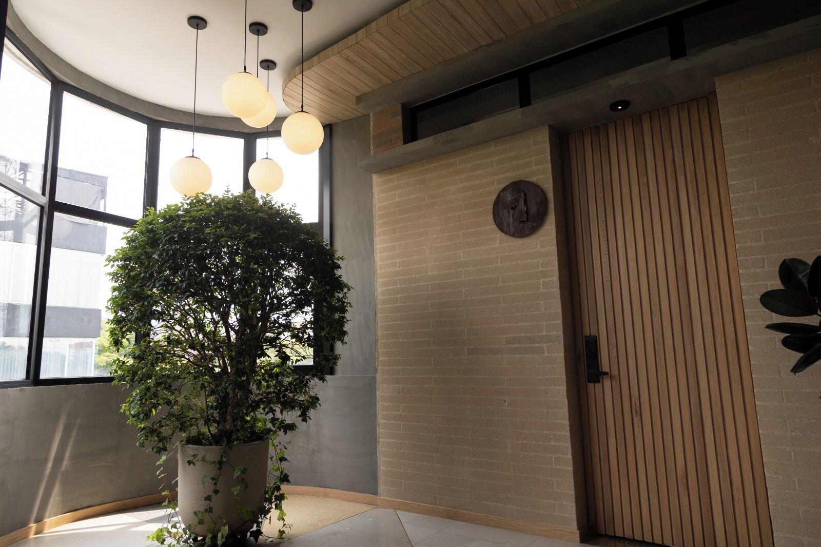 Un interior moderno con una planta en maceta grande, luces esféricas colgantes, una puerta de madera y una pared de ladrillo.