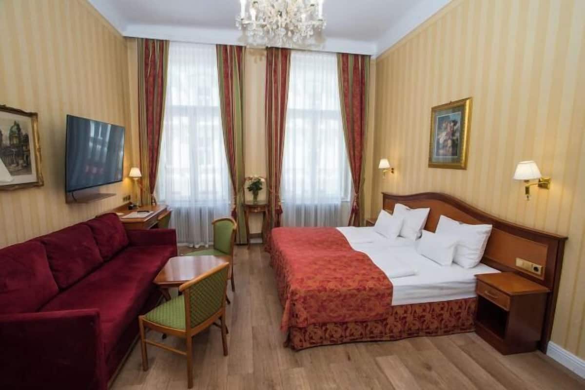 A hotel room with a bed, a sofa, a desk, and a television.