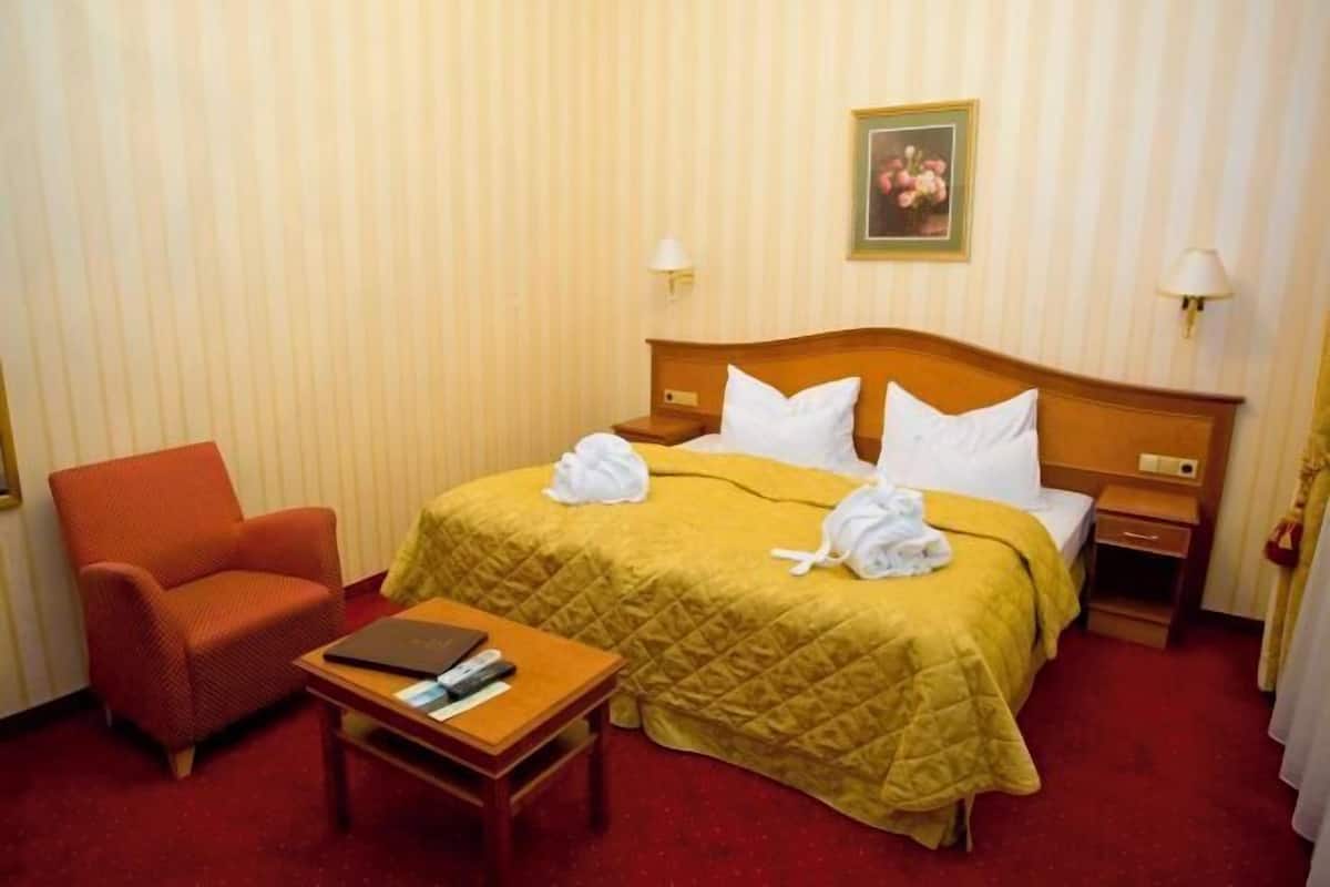 A hotel room with a bed, a chair, a small table, and a nightstand.