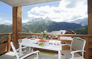 A wooden deck with a table and chairs, a potted plant, and a mountain view. - Residence Odalys Le Village de Praroustan (Uvernet-Fours)