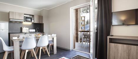 A modern kitchen with a dining area, a flat-screen TV, and a sliding glass door to a balcony.