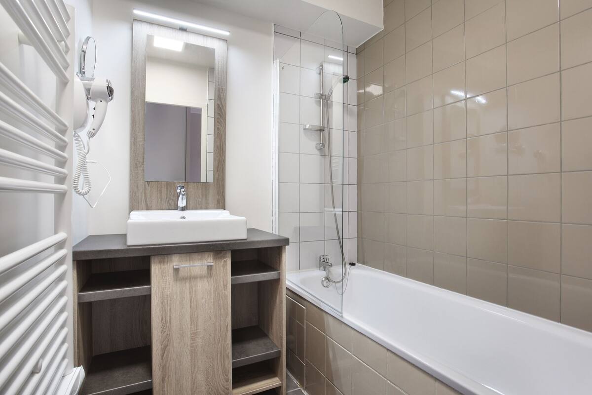Un baño moderno con lavamanos, espejo y ducha blancos.