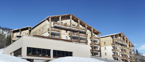 Un hotel de varios pisos con balcones, ventanas amplias y una pista de esquí al fondo.