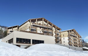 Un hôtel à plusieurs étages, doté de balcons, de grandes fenêtres et surplombant une piste de ski.