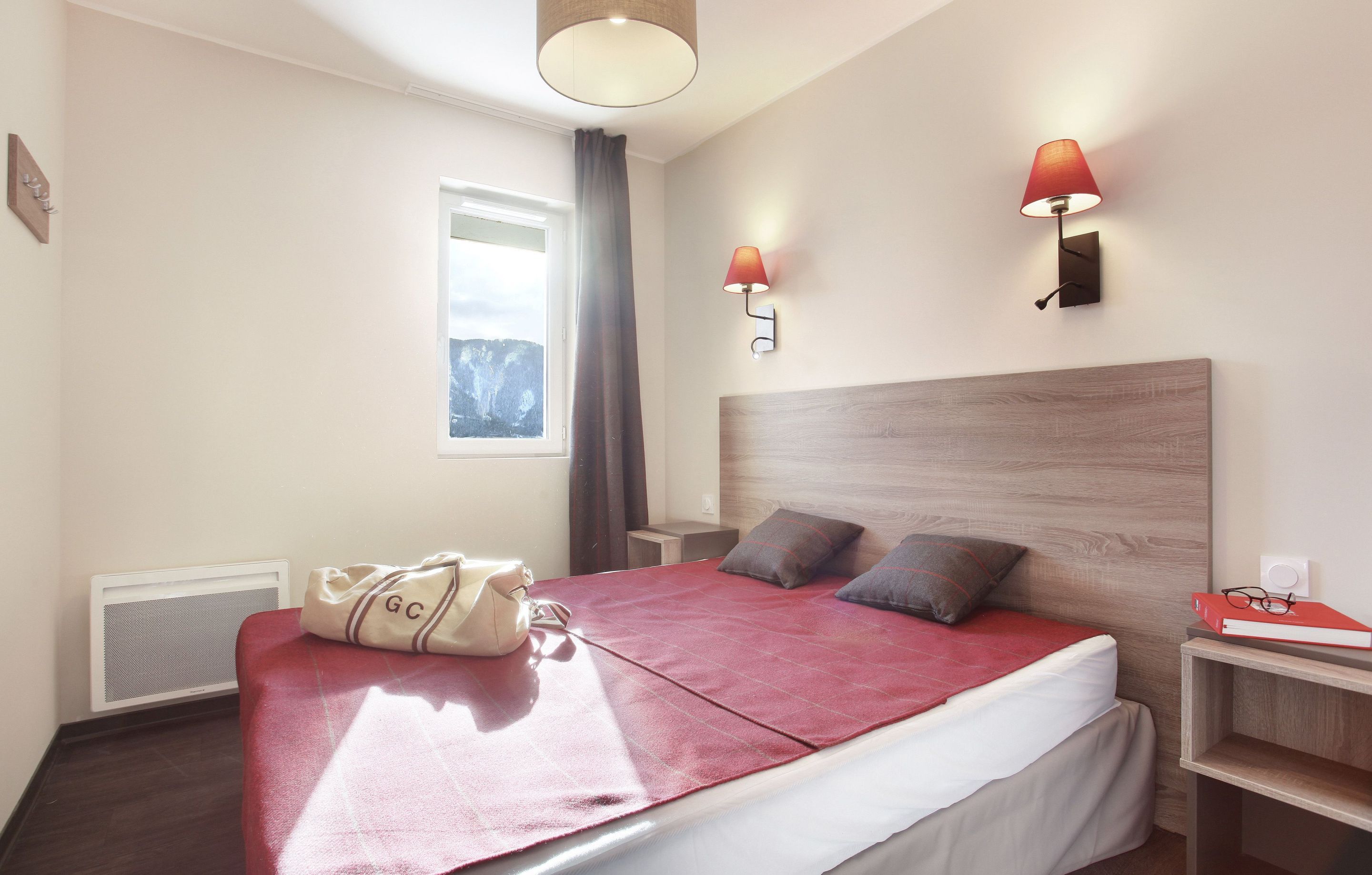 A hotel room with a bed, bedside lamps, a window, and a wall-mounted heater.