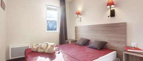 A hotel room with a bed, bedside lamps, a window, and a wall-mounted heater.