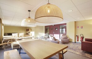 Habitación de hotel moderna con una gran mesa de madera, dos sofás cómodos, una mesa redonda de centro y una lámpara colgante de fibra trenzada.