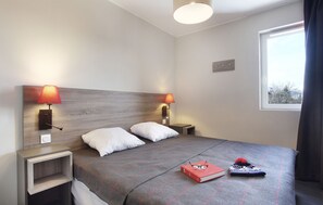 Una cama bien hecha con cubrecama escocés, dos lámparas de noche y una ventana con cortinas.