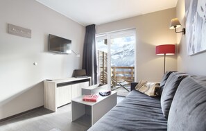 Una sala de estar moderna con un sofá, un televisor de pantalla plana, un escritorio y una ventana con vistas a las montañas.