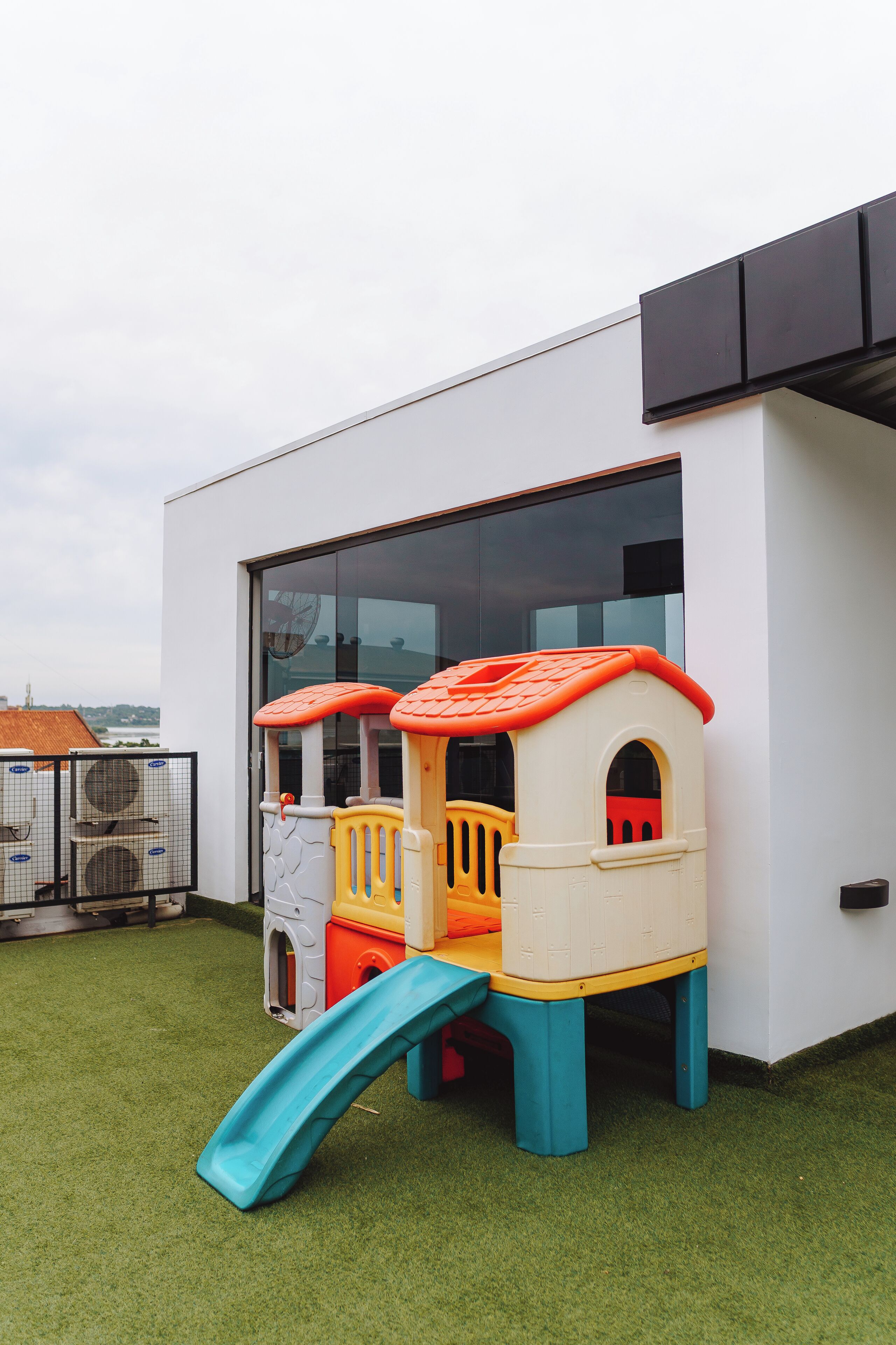Een speelruimte voor kinderen met een glijbaan en klimconstructies, gelegen op een dak met uitzicht over de stad.