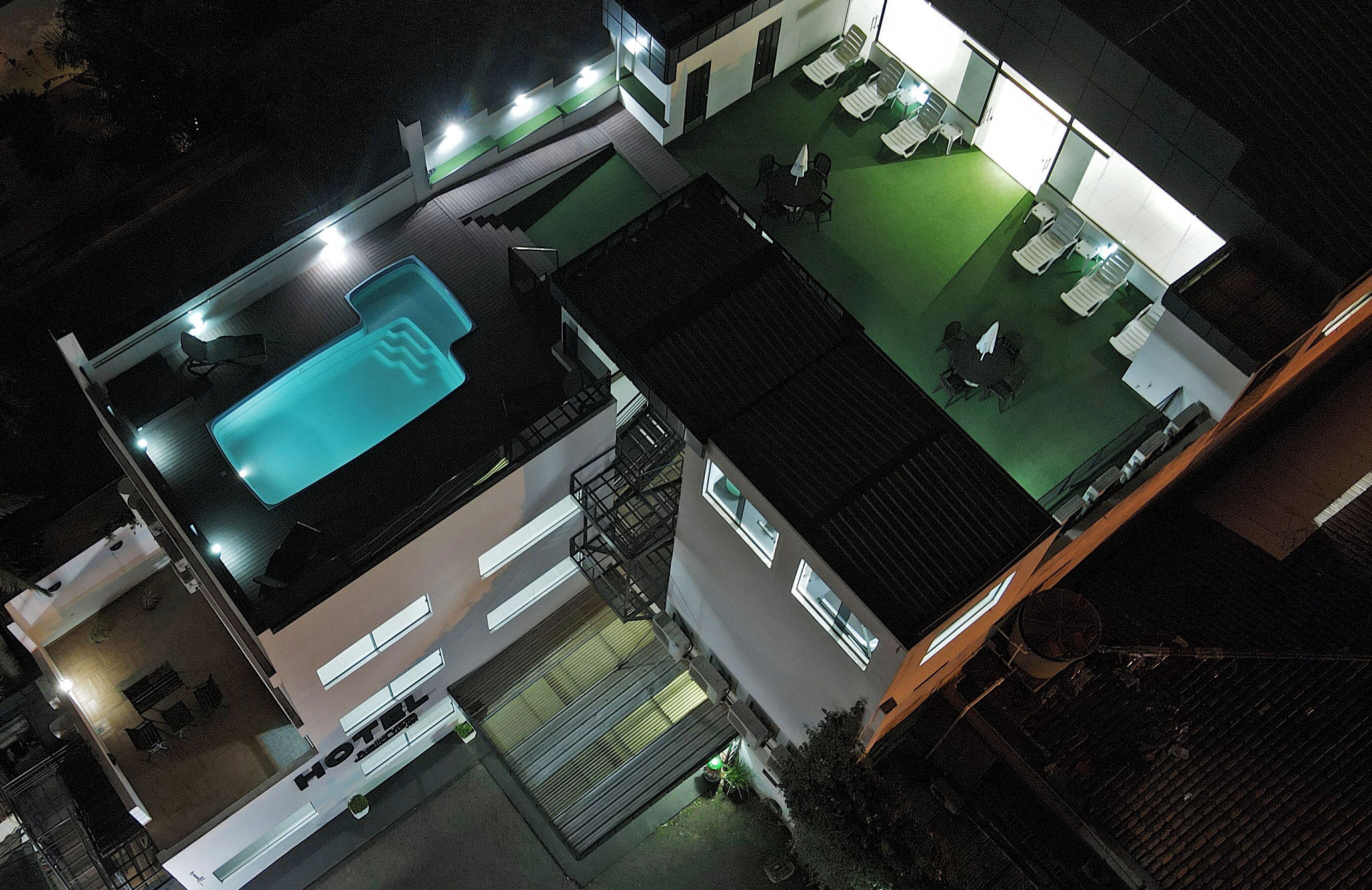 A rooftop pool with lounge chairs, a covered patio, and a building with a flat roof.