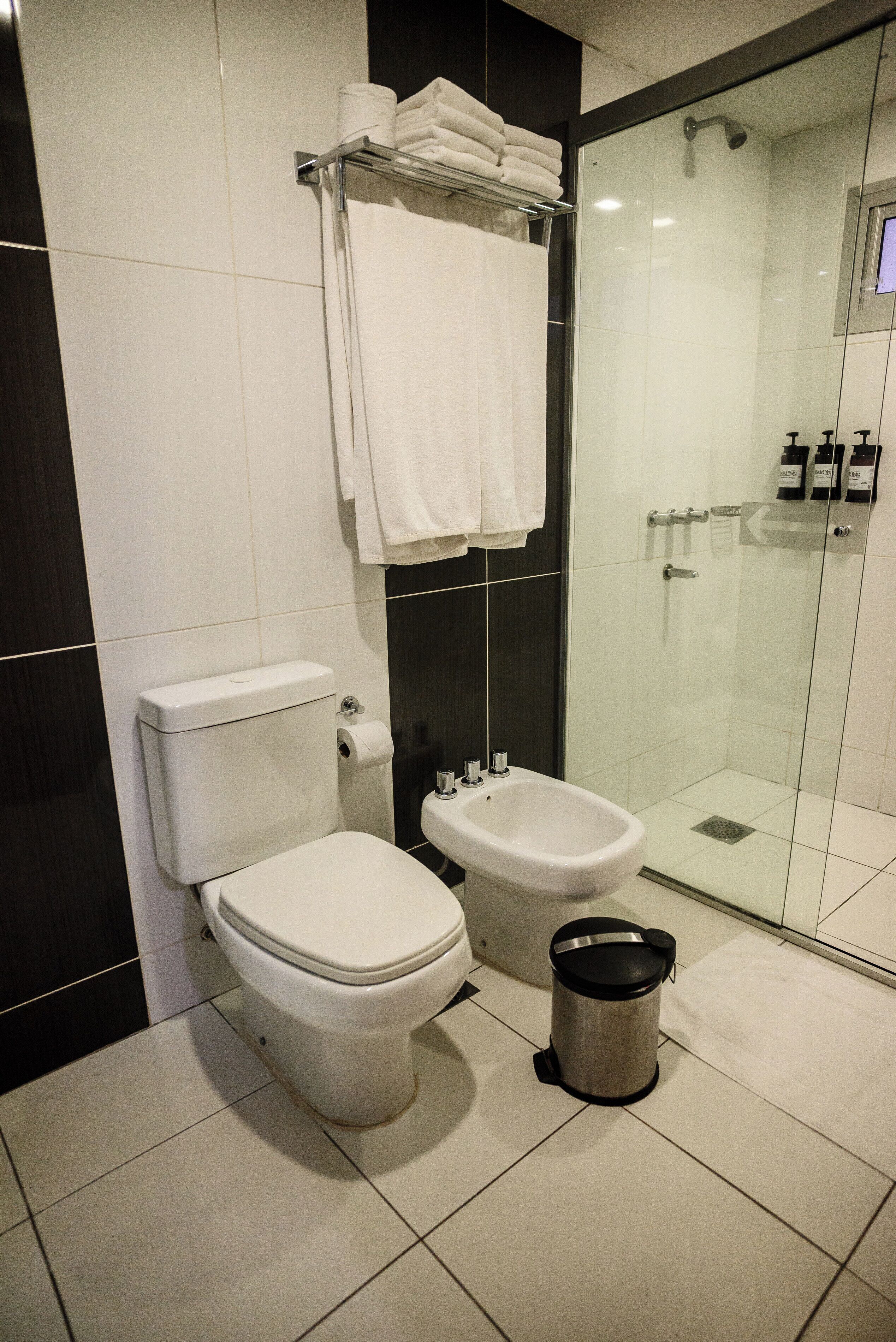 Baño con inodoro, bidé y zona de ducha con mampara de vidrio.