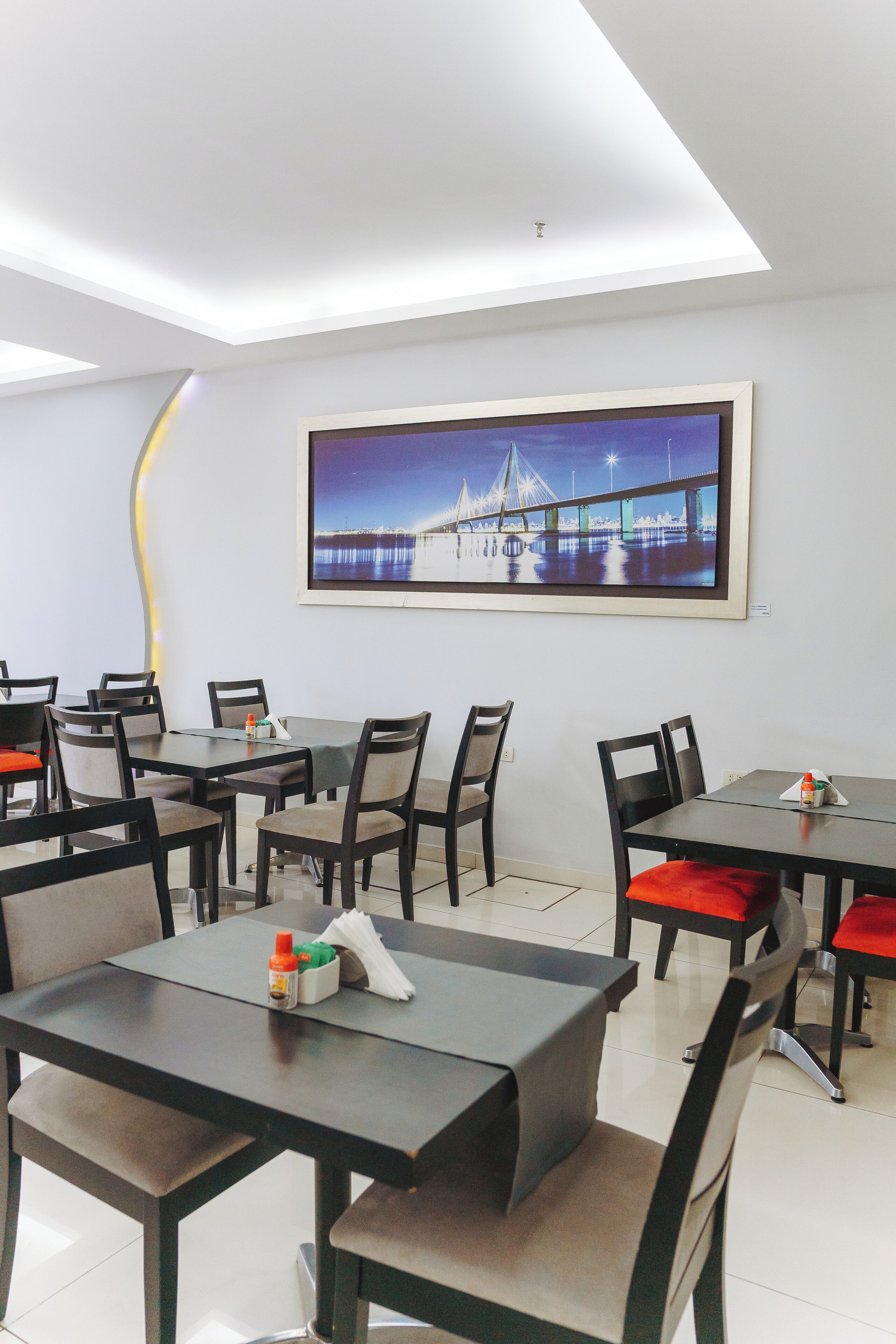 A modern dining area with tables and chairs, a large framed picture on the wall, and a unique ceiling design.