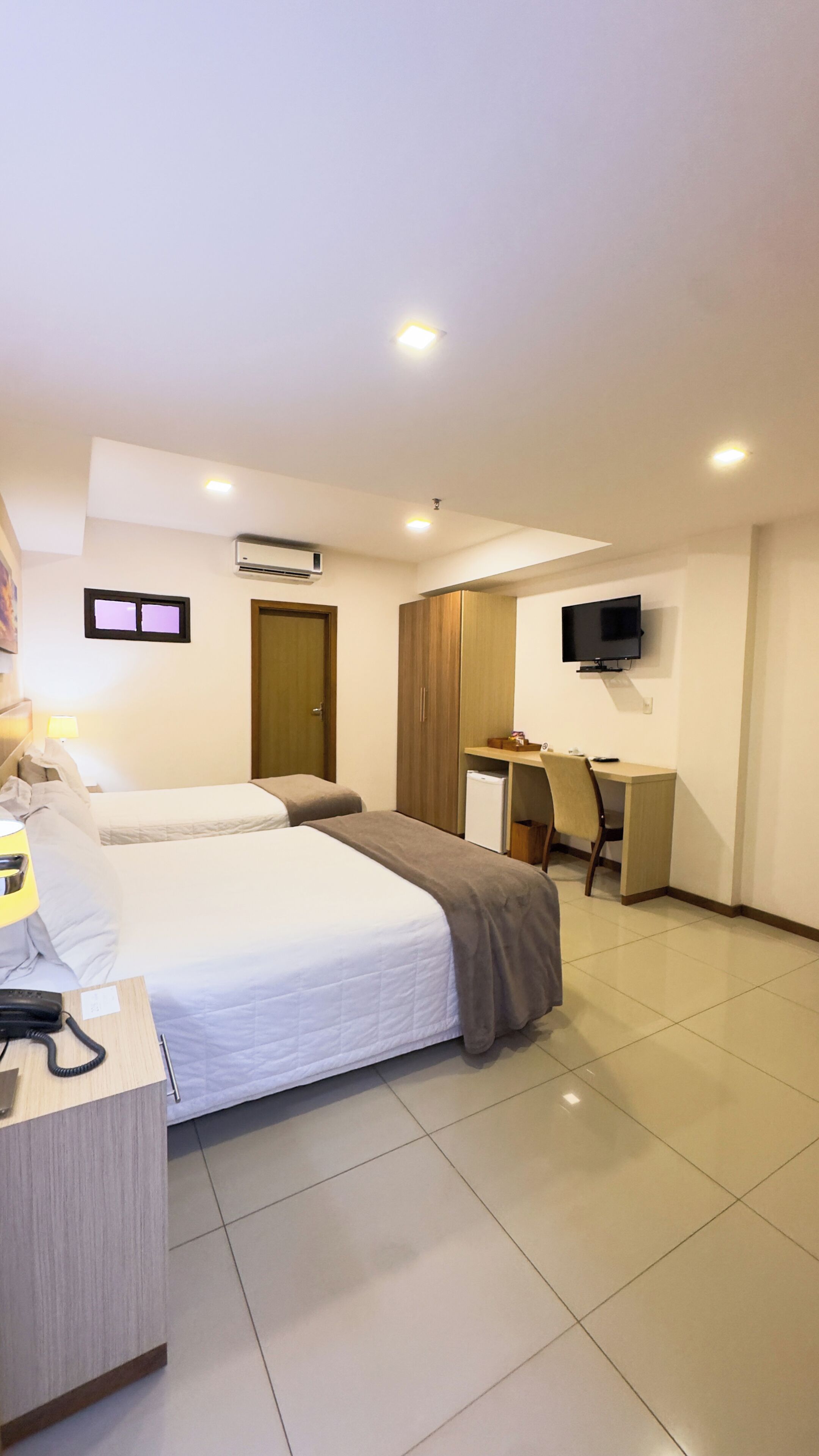 A hotel room with two beds, a desk, a chair, a television, an air conditioning unit, and a telephone.