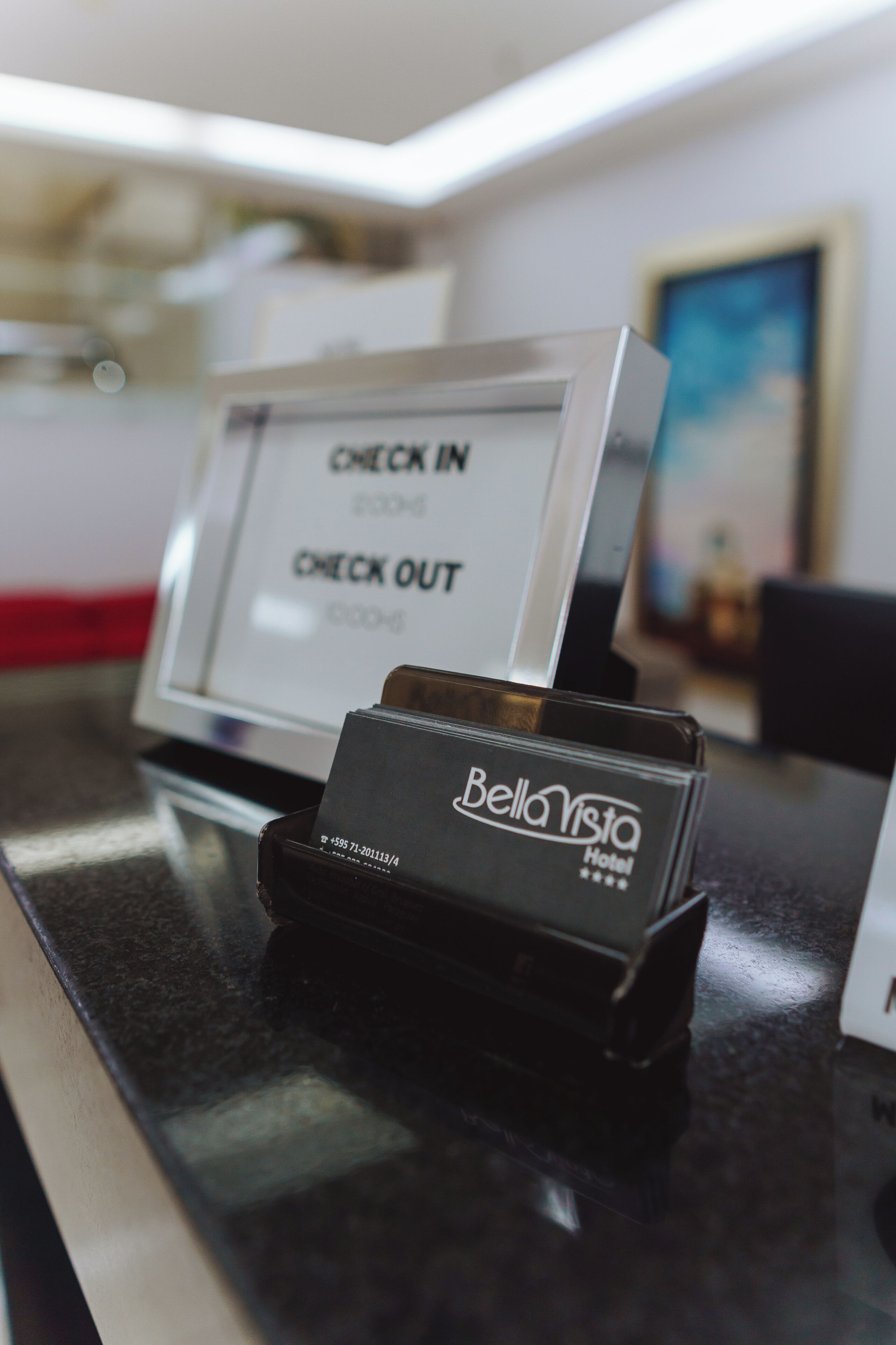 A hotel reception desk with a check-in/check-out counter, a card reader, and a framed picture on the wall.