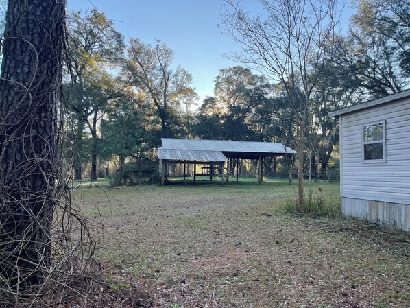 A rustic cabin with a metal roof and wooden structure, surrounded by trees and a grassy area.