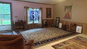Ein Wohnzimmer mit großem Fenster, einem Holzschrank, einem braunen Sessel und einem gemusterten Teppich.