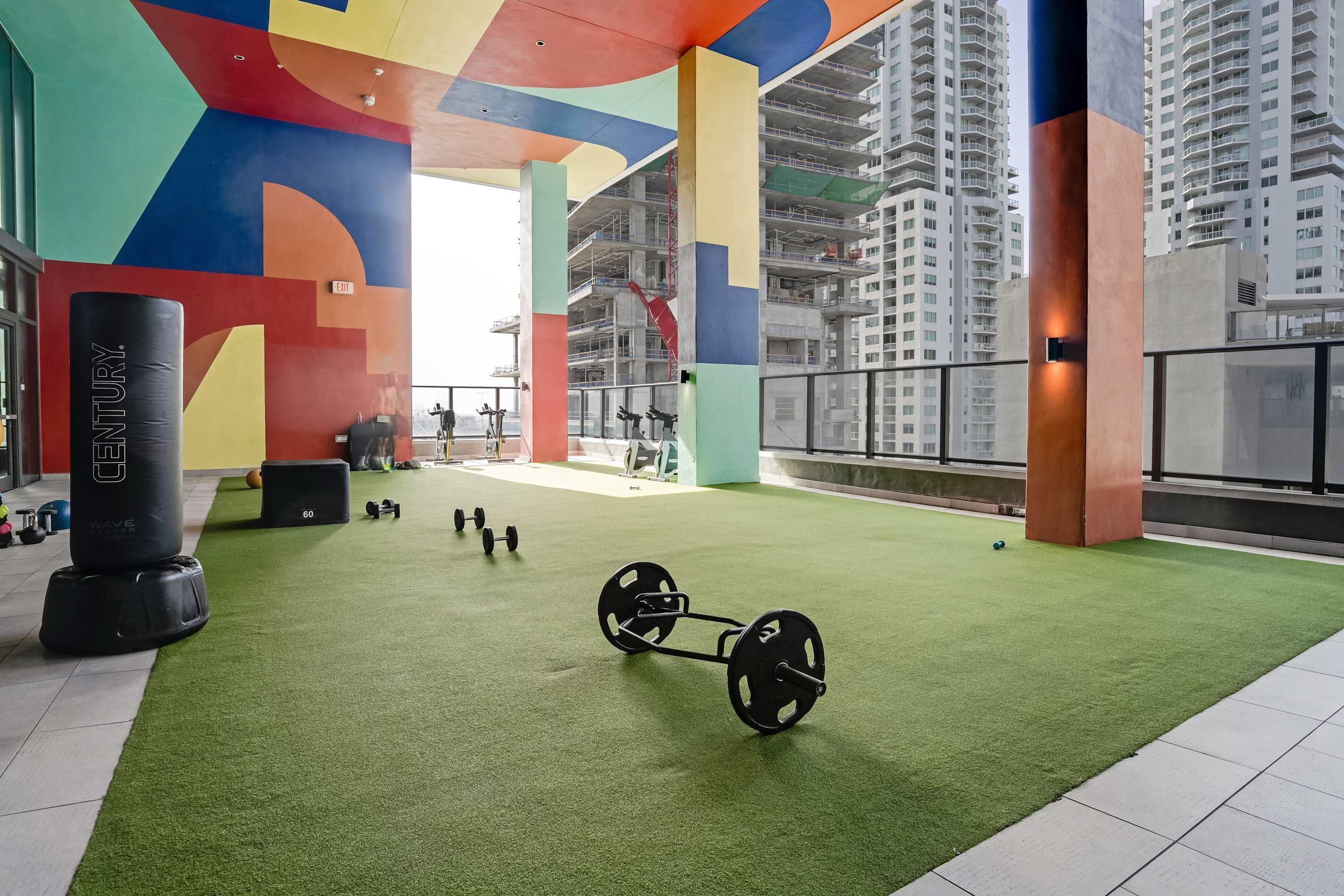 Une salle de sport dotée d’un sol en gazon synthétique vert, d’équipements de musculation et de décorations murales abstraites et colorées.